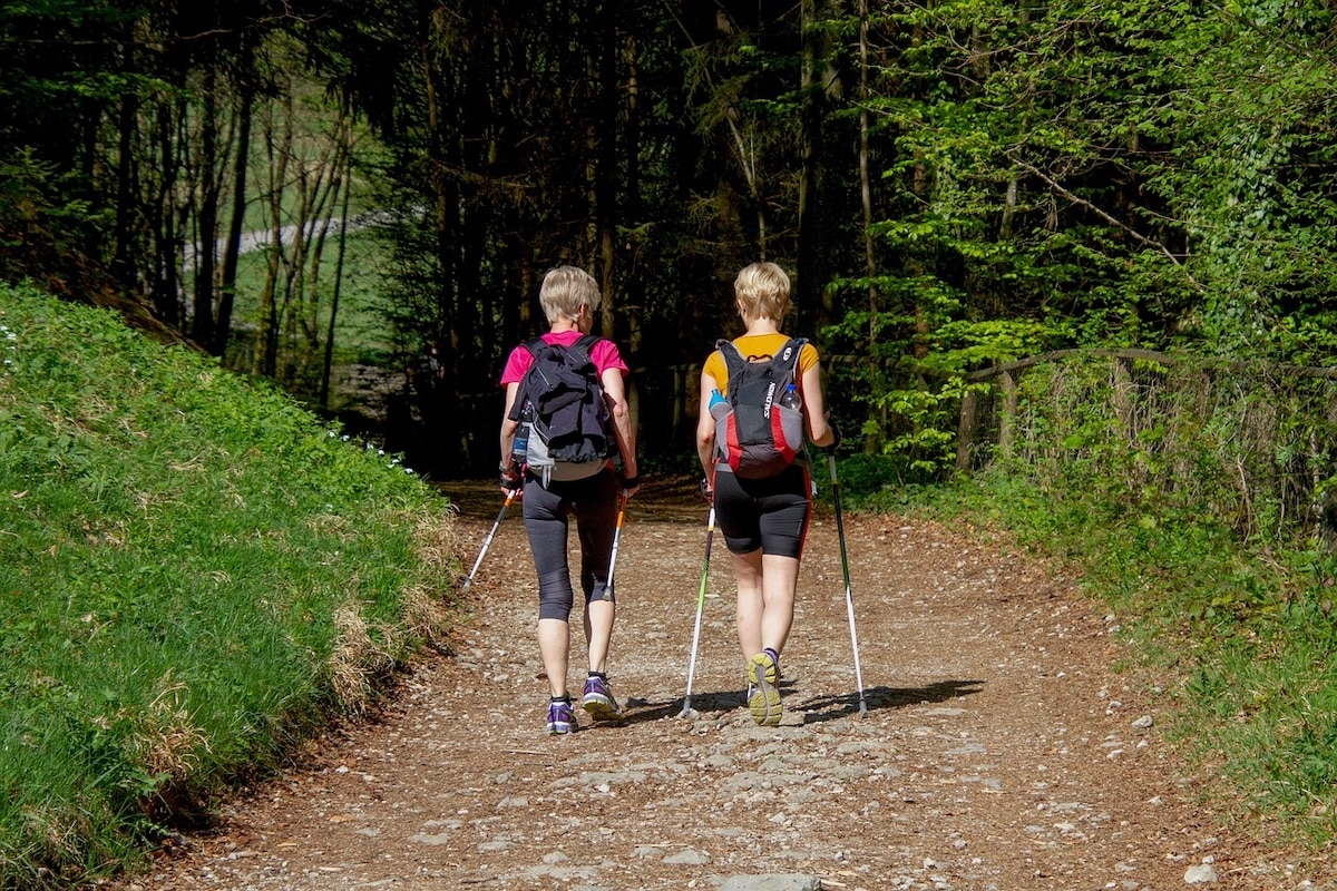 Two women hike along a dirt path with the help of hikers' walking sticks. Walking is an easy way to improve your health and reduce stress.